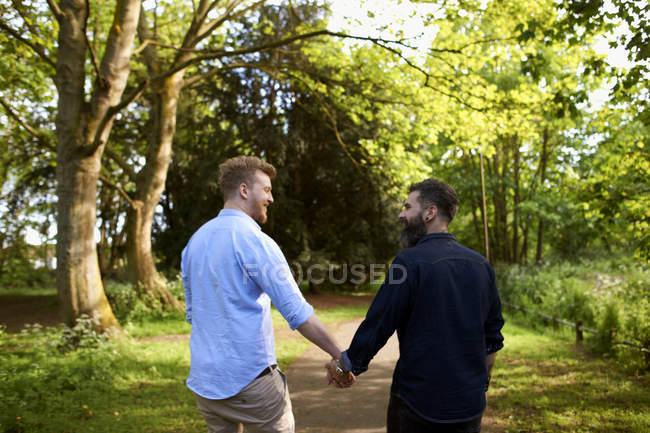 Afectuosa pareja gay masculina cogida de la mano en el soleado parque - foto de stock