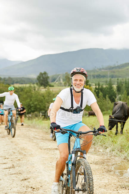 Усміхнений, впевнений зрілий чоловік гірський велосипед на сільській брудній дорозі — стокове фото