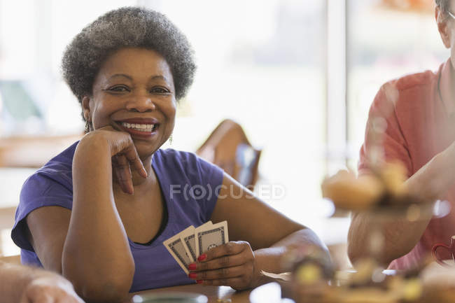 Retrato sonriente, mujer mayor confiada jugando a las cartas en el centro comunitario - foto de stock