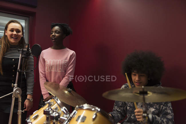 Músicos adolescentes grabando música, cantando y tocando la batería en la cabina de sonido - foto de stock