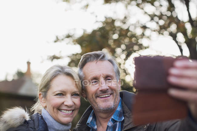 Mature caucasian couple taking photo on smartphone at autumn park — Stock Photo
