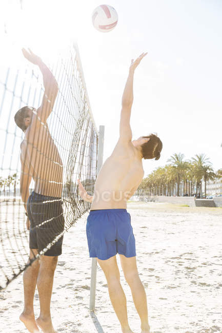 Uomini che giocano a beach volley sulla spiaggia soleggiata — Foto stock