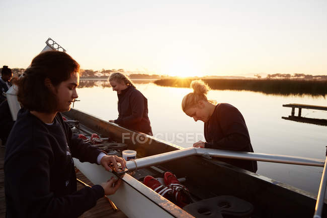 Female rowers preparing scull at sunrise lakeside — Stock Photo