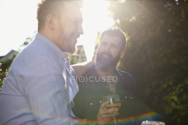 Любящие гей-пары пьют вино в солнечном саду — стоковое фото