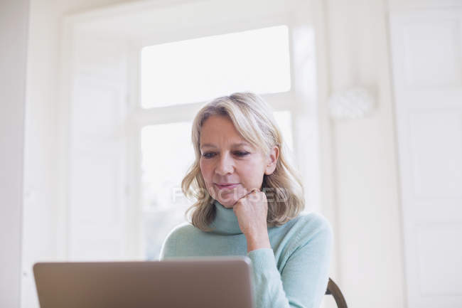 Freelancer feminino maduro focado trabalhando no laptop em casa — Fotografia de Stock