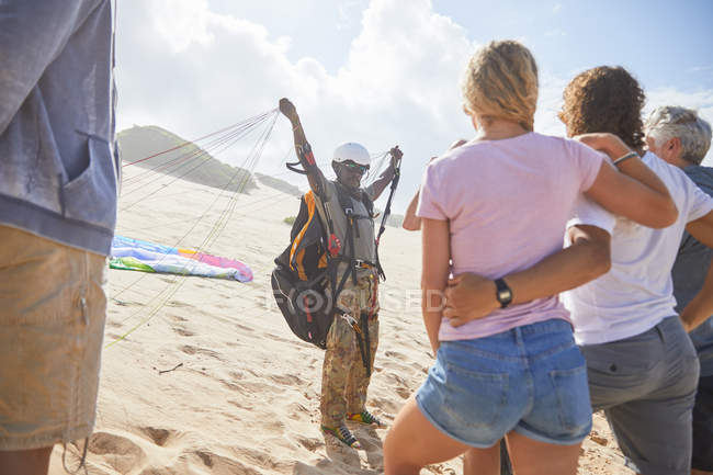 Studenti che guardano istruttore di parapendio maschile con attrezzatura sulla spiaggia soleggiata — Foto stock
