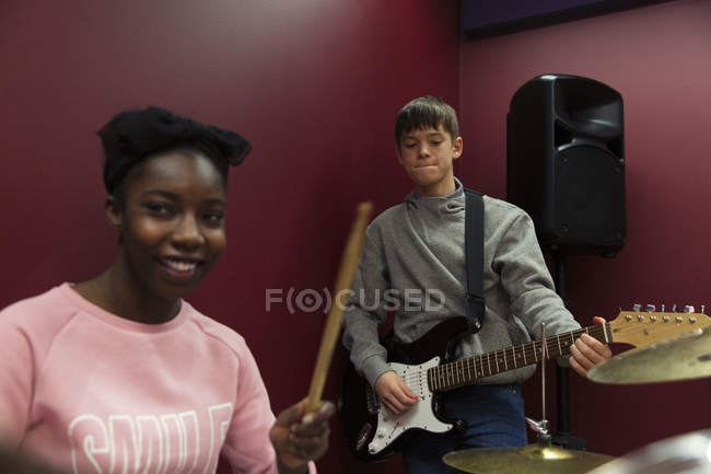 Sonrientes músicos adolescentes grabando música, cantando y tocando guitarra eléctrica en cabina de sonido - foto de stock