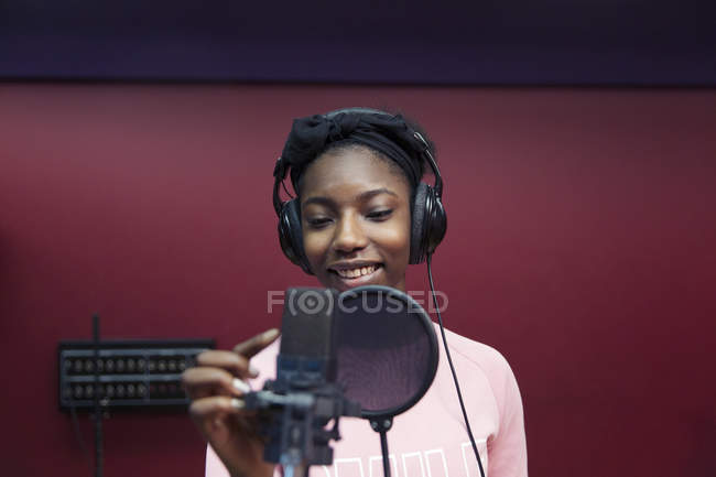 Smiling teenage girl musician recording music, singing in sound booth — Stock Photo