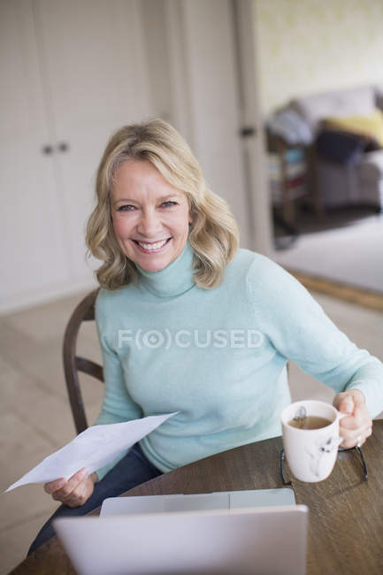 Retrato sonriente, mujer independiente confiada trabajando en el portátil y bebiendo té en casa - foto de stock