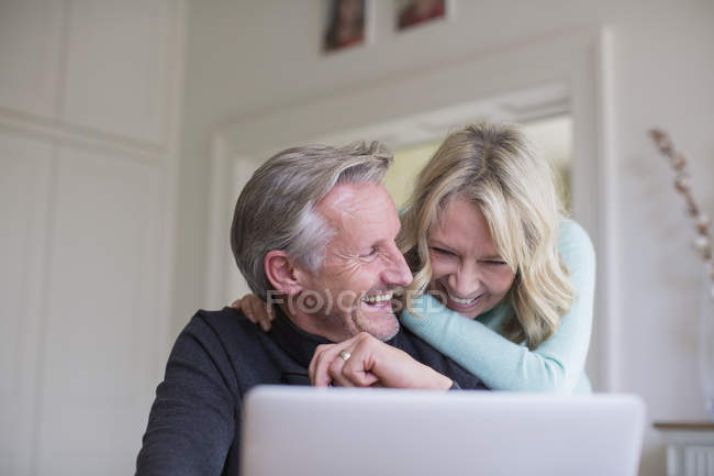 Riendo, pareja madura despreocupada usando el ordenador portátil - foto de stock