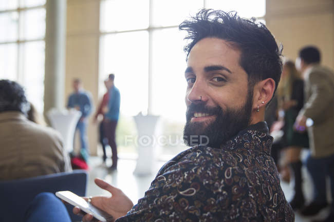Retrato sorridente empresário com barba usando telefone inteligente no público da conferência — Fotografia de Stock