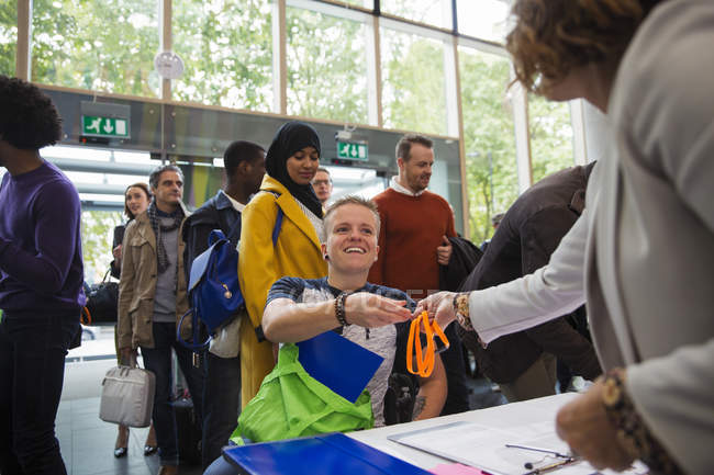 Улыбающаяся женщина в инвалидной коляске прибывает и регистрируется за столом регистрации конференции — стоковое фото