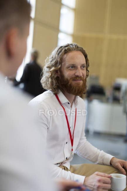 Smiling businessman drinking coffee at conference — Stock Photo