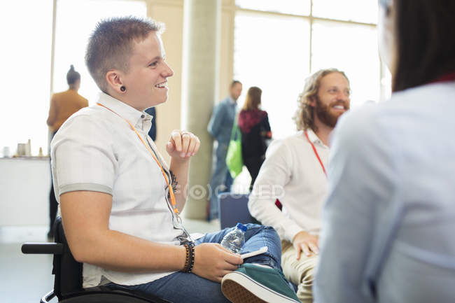 Усміхнена жінка в інвалідному візку розмовляє з колегами на конференції — стокове фото