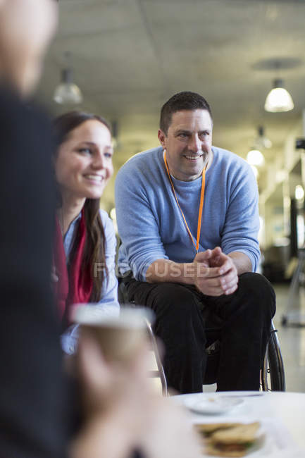 Улыбающийся бизнесмен в сети инвалидных колясок, разговаривающий с коллегами — стоковое фото