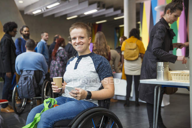 Retrato sonriente, mujer segura en silla de ruedas usando el teléfono inteligente en la conferencia - foto de stock