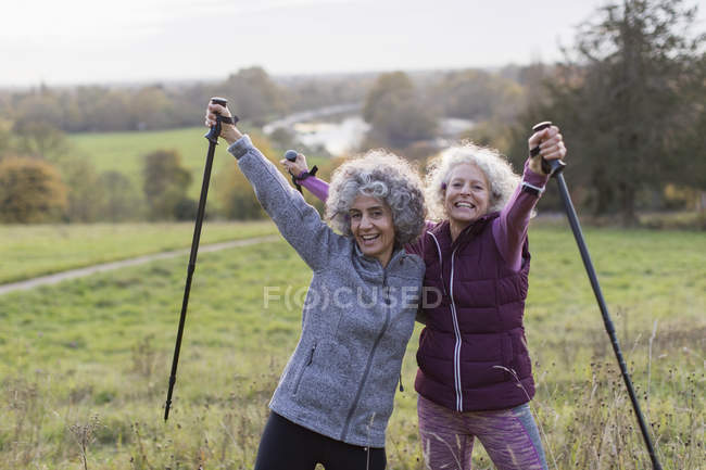 Portrait enthusiastic, confident active senior women friends hiking with poles in rural field — Stock Photo