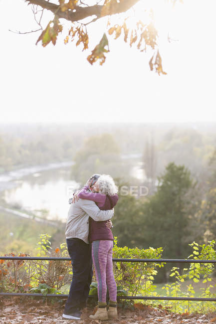 Affectionate active senior couple hugging in sunny autumn park — Stock Photo