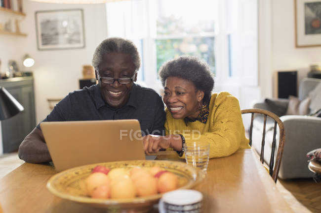 Senior couple using laptop at dining table — Stock Photo