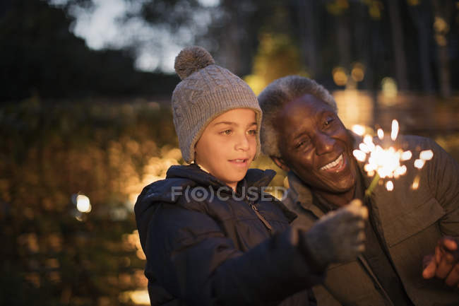 Abuelo y curioso nieto jugando con bengalas de fuegos artificiales - foto de stock