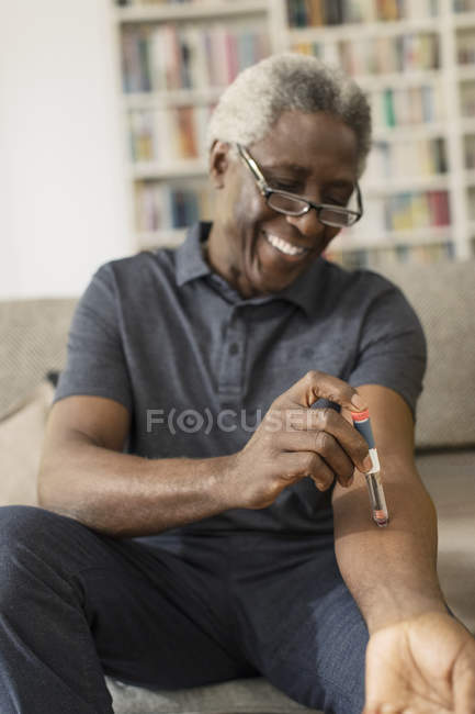 Hombre mayor sonriente tomando insulina en casa - foto de stock