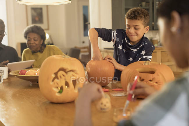 Мальчик вырезает тыквы на Хэллоуин за столом — стоковое фото