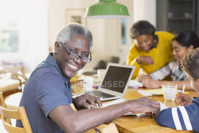 Портрет улыбающегося, уверенного в себе пожилого человека, пользующегося ноутбуком с семьей — стоковое фото