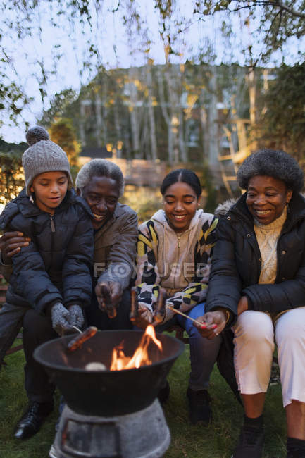 Abuelos y nietos asando perritos calientes sobre fogata - foto de stock