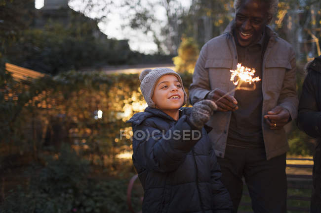 Nieto sonriente y abuelo jugando con bengalas de fuegos artificiales - foto de stock