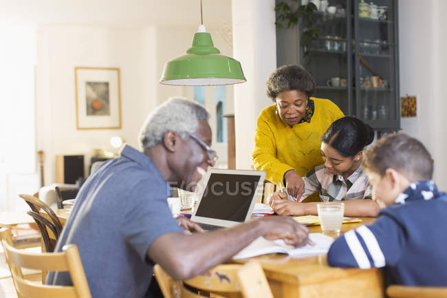 Avós ajudando netos com trabalhos de casa na mesa de jantar — Fotografia de Stock