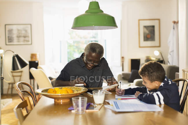Grandfather at dining table with grandson doing homework — Stock Photo