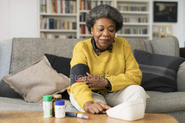 Mulher sênior verificando a pressão arterial na sala de estar — Fotografia de Stock
