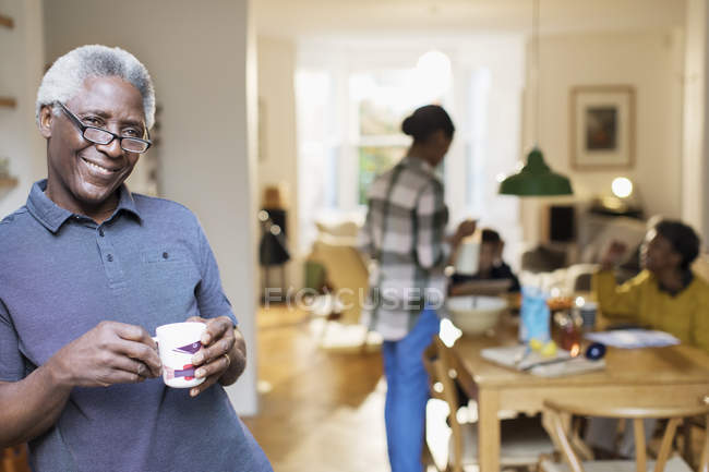 Portrait smiling, confident senior man drinking coffee with family in background — Stock Photo