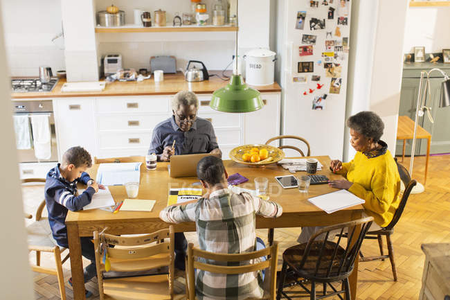 Бабусі і дідусі за обіднім столом з онуками роблять домашнє завдання — стокове фото