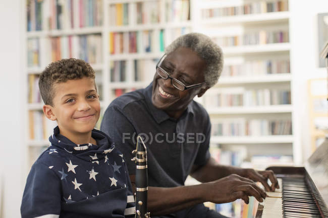 Портрет улыбающийся, уверенный дедушка и внук, играющие на пианино и кларнете — стоковое фото