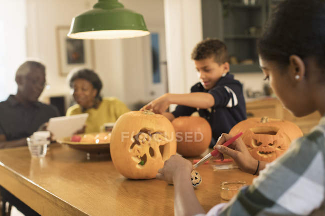 Abuelos en la mesa con nietos tallando calabazas de Halloween - foto de stock