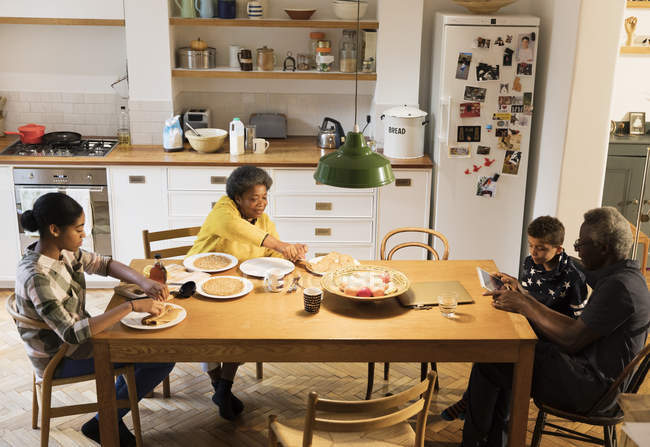 Бабушки и внуки едят и используют цифровые планшеты за обеденным столом — стоковое фото