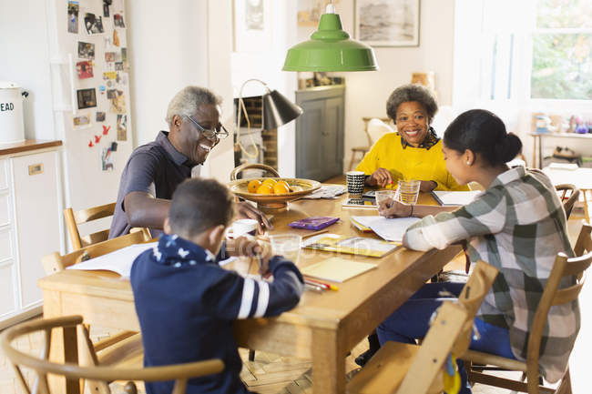 Бабусі і дідусі за обіднім столом з онуками роблять домашнє завдання — стокове фото