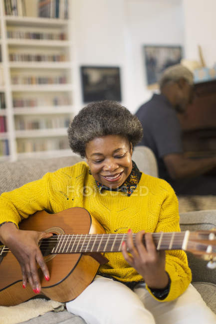 Улыбающаяся пожилая женщина играет на гитаре на диване — стоковое фото