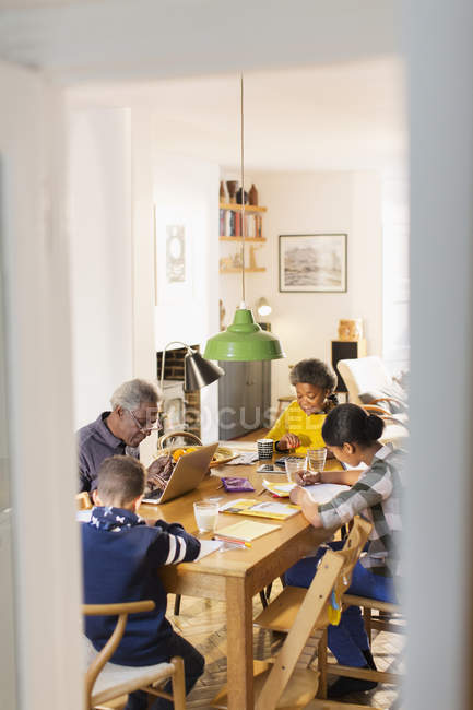 Avós na mesa de jantar com netos fazendo lição de casa — Fotografia de Stock