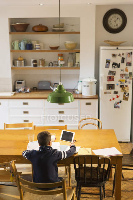 Visão traseira do menino fazendo lição de casa na mesa de jantar — Fotografia de Stock