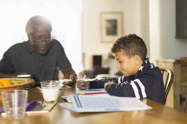 Grandfather at table with grandson doing homework — Stock Photo