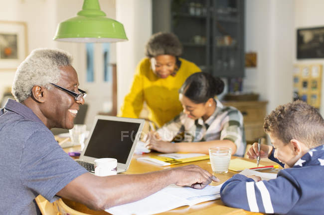 Grandfather helping grandson with homework at dining table — Stock Photo