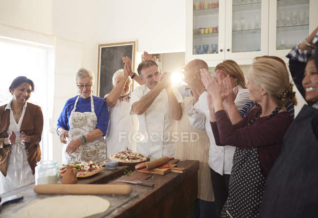 Chef y amigos mayores activos aplaudiendo en la clase de cocina de pizza - foto de stock