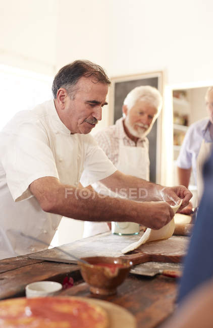 Chef enfocado esparciendo masa de pizza en clase de cocina - foto de stock