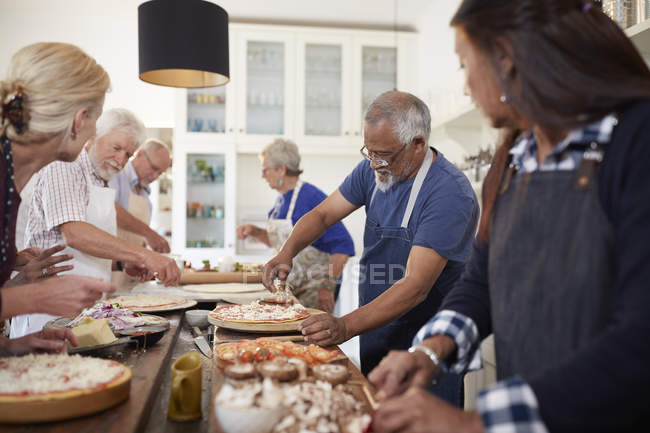 Amigos seniores fazendo pizzas na aula de culinária — Fotografia de Stock
