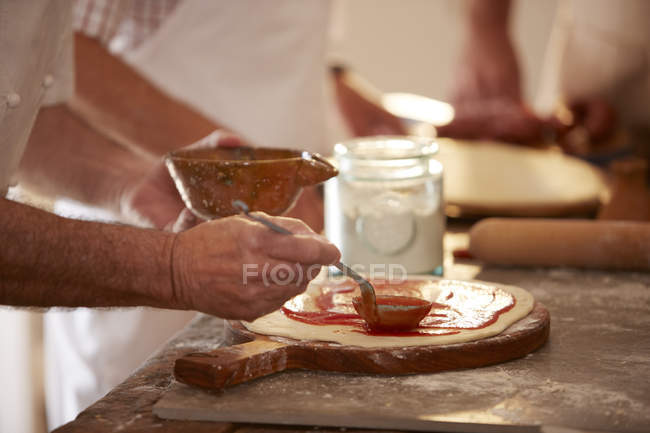 Gros plan homme propagation sauce marinara sur la pâte dans le cours de cuisine de pizza — Photo de stock