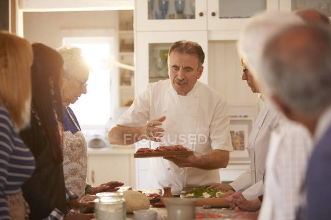 Amigos mayores escuchando al chef en la clase de cocina de pizza - foto de stock