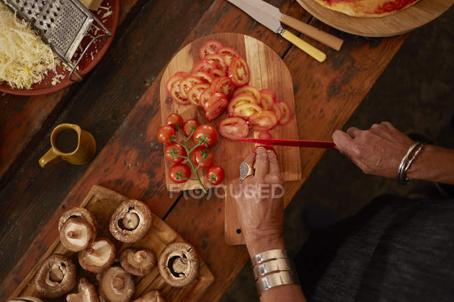 Overhead view woman slicing fresh tomatoes for pizza — Stock Photo