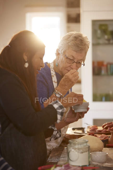 Mujeres mayores amigas oliendo queso fresco en la clase de cocina de pizza - foto de stock